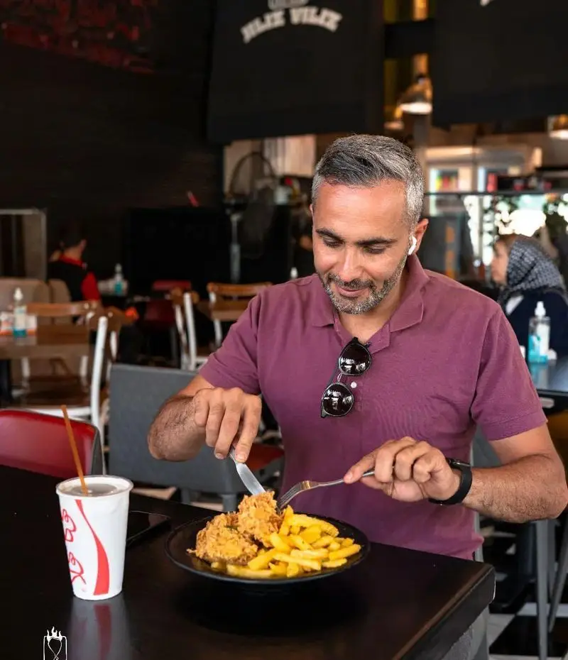 مشتری مردی در حال لذت بردن از غذای خوشمزه مرغ سوخاری و سیب‌زمینی سرخ کرده در محیط دلنشین فست فود جیلیزویلیز شعبه پیروزی.