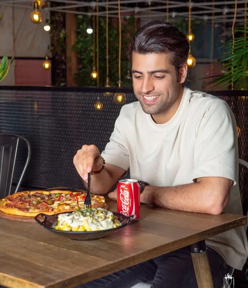 مردی خوشحال در فست فود جیلیزویلیز پیروزی در حال لذت بردن از پیتزا و سیب زمینی با سس در محیطی دلنشین و مدرن.