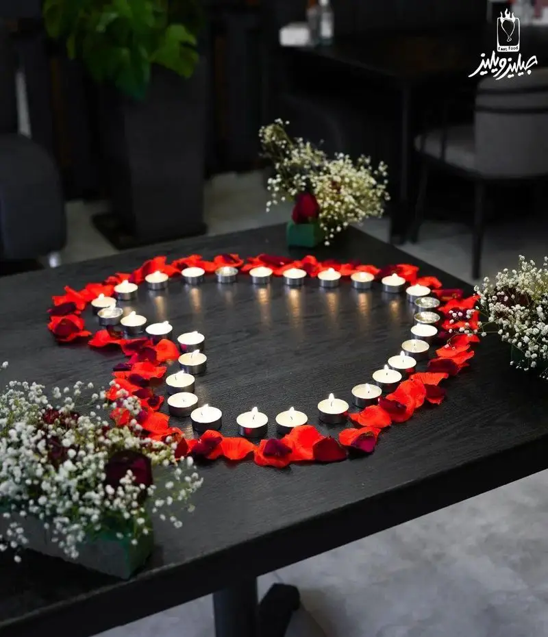 میز آرایی رمانتیک در فست فود جیلیزویلیز پیروزی با شمع های نورانی، گلبرگ های قرمز و گل برای شام عاشقانه.