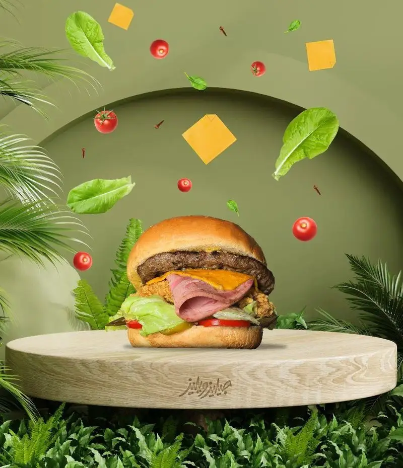 برگر سوپر میکس از فست فود جیلیزویلیز پیروزی با لایه‌های گوشت، مرغ سوخاری، ژامبون، پنیر، کاهو و گوجه در پس‌زمینه سبز جنگلی