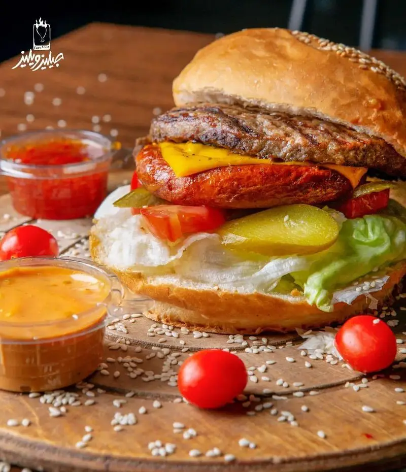 تصویری جذاب از برگر مخصوص جیلیزویلیز پیروزی؛ ترکیبی از گوشت، سوسیس، پنیر، کاهو و گوجه در محیطی دلنشین.