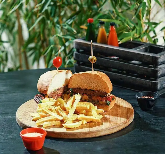 برگرهای خوشمزه و سیب زمینی سرخ کرده در کافه هاگ. دو برگر با نان تازه و مخلفات به همراه سس‌های رنگارنگ و میز چوبی کافه.