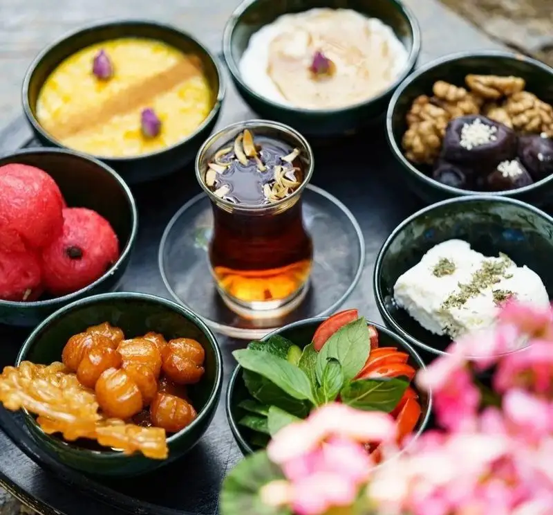 تصویری از میز صبحانه کامل کافه هاگ: چای، پنیر، خرما، گردو، میوه تازه، شیرینی بامیه و شله‌زرد سنتی ایرانی.