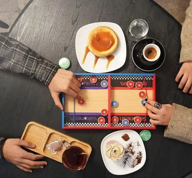 دو نفر در کافه هاگ در حال بازی رومیزی سرگرم‌کننده، همراه با لذت دسر، قهوه اسپرسو و چای. فضایی دلنشین برای دورهمی.