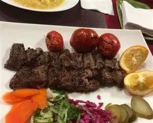 تصویر یک بشقاب کباب اصیل عشایر کباب با تکه‌های کباب گوشت، گوجه کبابی، لیمو و سبزیجات تازه. بهترین غذای سنتی ایرانی.