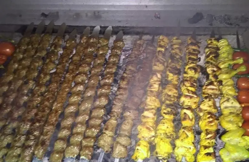 تصویری جذاب از انواع کباب های تازه و خوشمزه، شامل کباب کوبیده و جوجه کباب، آماده شده در کبابی عشایر کباب بر روی منقل داغ، همراه با گوجه کبابی. تجربه غذای اصیل ایرانی.