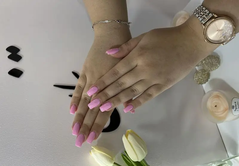 طراحی و کاشت ناخن دخترانه با لاک صورتی ملایم و شیک به همراه اکسسوری ساعت مچی زنانه طلایی و دستبند نقرهای ظریف