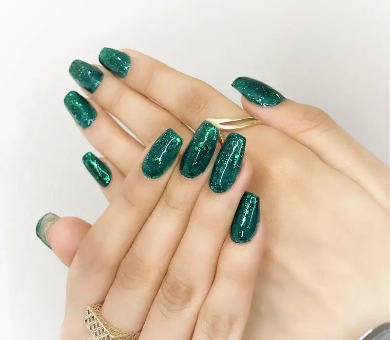 طراحی و کاشت ناخن مجلسی با لاک ژل سبز تیره اکلیلی و شیک به همراه انگشترهای طلایی زنانه در سالن زیبایی تخصصی ناخن
