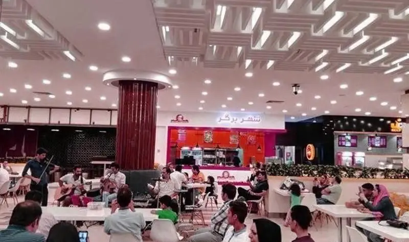 تصویر فست فود شهربرگر با مشتریان در حال غذا خوردن، اجرای زنده موسیقی با ویولن و گیتار و فضای داخلی مدرن و روشن.