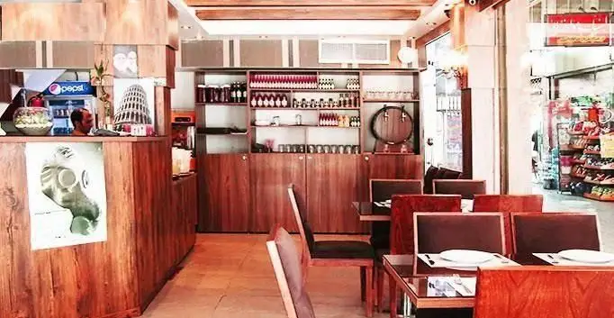 نمای داخلی رستوران ایران ایتالیا، دکوراسیون چوبی با میزهای قهوه‌ای، بوفه نوشیدنی و محیطی دلنشین برای مشتریان.