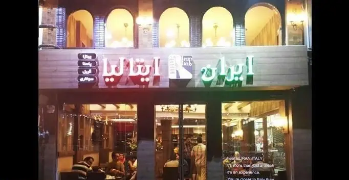 نمای بیرونی رستوران ایران ایتالیا با تابلوهای روشن و منوی پیتزا و پاستا. فضایی دلنشین برای تجربه طعم‌های اصیل ایتالیایی در تهران.