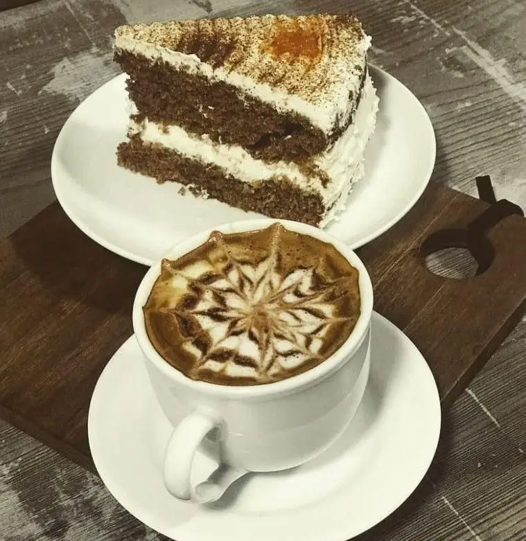 کیک لایه‌ای اشتهاآور با رویه خامه و پودر کاکائو، به همراه لاته آرت زیبای ستاره‌ای. بهترین انتخاب کافه آفر برای لحظات شیرین.