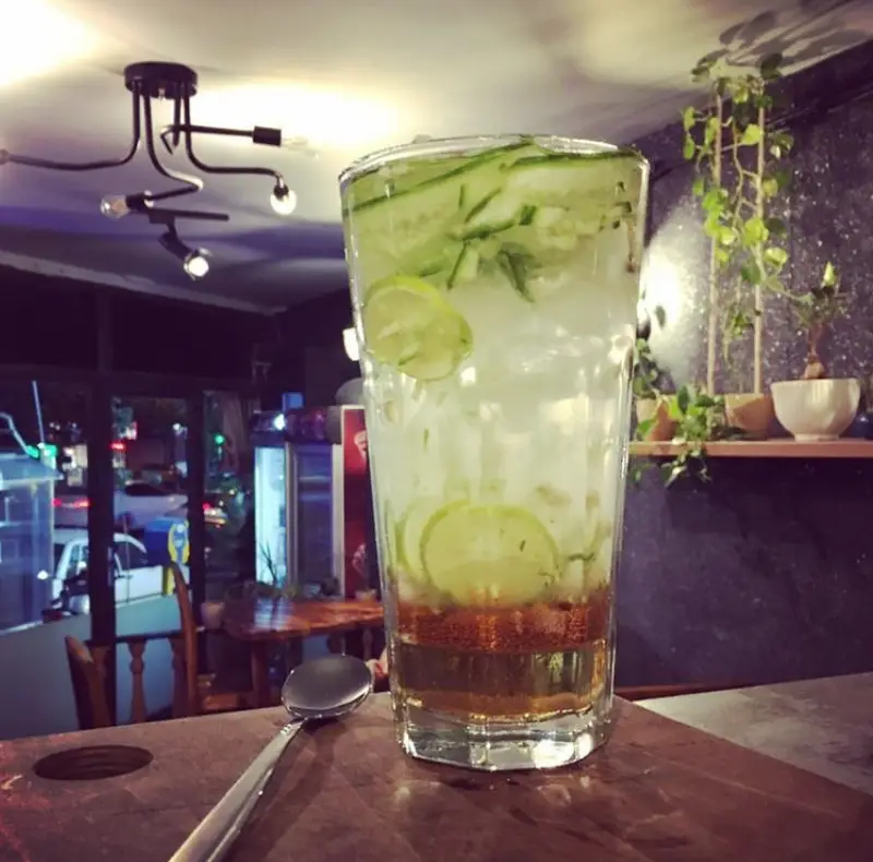 نوشیدنی خنک و گوارا با برش‌های لیمو و خیار و یخ در یک لیوان بلند در کافه آفر. دکوراسیون زیبای داخلی با لوستر و گیاهان.