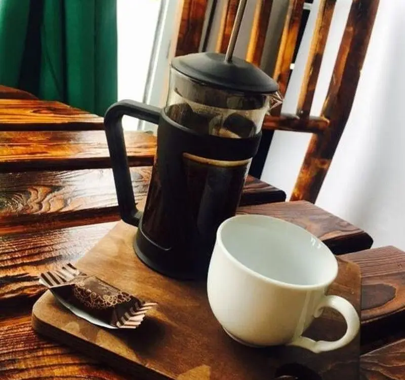 تجربه لذت‌بخش نوشیدن قهوه داغ و تازه با فرنچ پرس در محیط دلنشین کافه آفر؛ همراه با فنجان سفید و شکلاتی خوشمزه برای شروعی عالی.