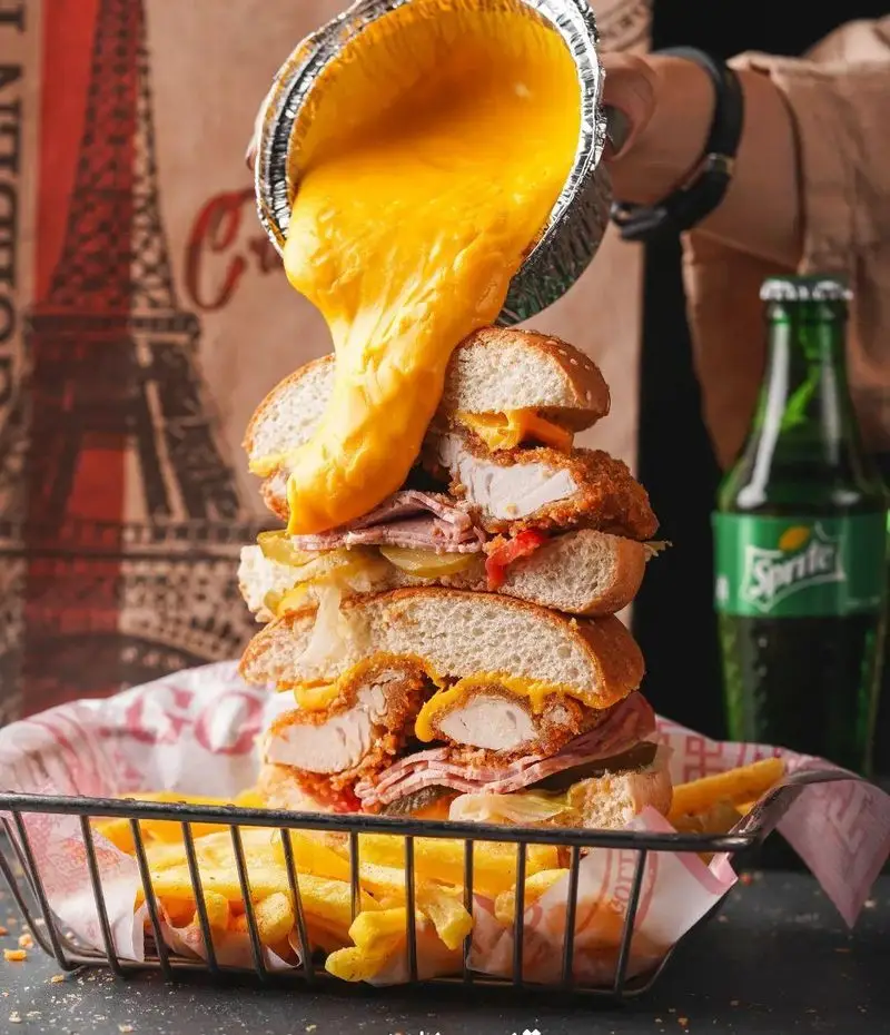 یک ساندویچ برج فست فود قلب طلایی نیاوران با فیله مرغ، ژامبون، ترشی و غرق در سس پنیر داغ، سرو شده با سیب زمینی.