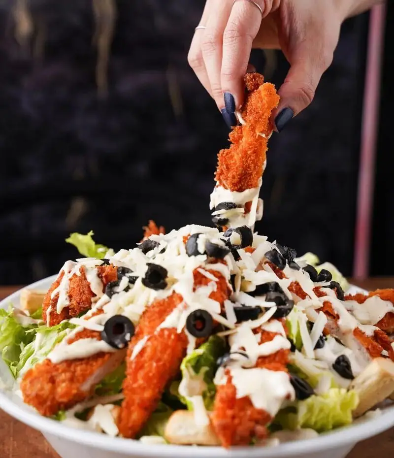 سالاد سزار مرغ سوخاری خوشمزه از فست فود قلب طلایی نیاوران. دستی در حال افزودن مرغ سوخاری به سالاد تازه با زیتون و پنیر.