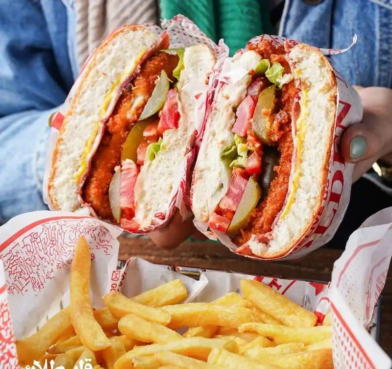 ساندویچ مرغ سوخاری پر و خوش‌رنگ فست فود قلب طلایی نیاوران، همراه با کاهو، خیارشور، گوجه و سیب‌زمینی سرخ‌کرده ترد و طلایی.