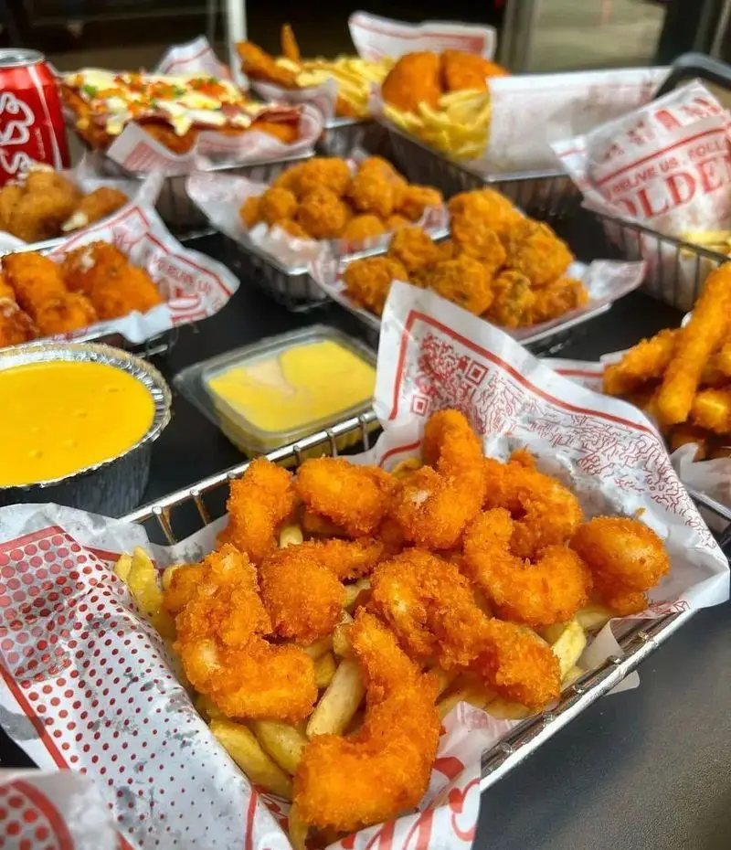 میز پر از غذاهای لذیذ فست فود قلب طلایی نیاوران: میگو سوخاری، سیب زمینی، مرغ سوخاری، ناگت و سس‌های مخصوص. تصویری جذاب از منوی متنوع.