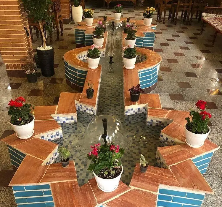فضای دلنشین رستوران سنتی آرامش با حوض آبی زیبا، فواره، گل و گلدان‌های رنگارنگ؛ دکوری آرامش‌بخش و سنتی.