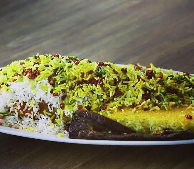 غذای پرطرفدار ایرانی رستوران نایب: زرشک پلو با برنج سفید و زعفرانی، تزیین شده با زرشک و سبزیجات معطر، همراه با بادمجان سرخ شده.