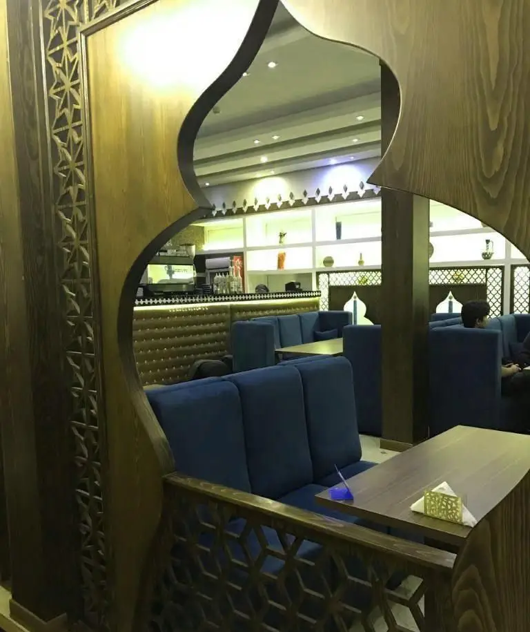 نمایی از دکوراسیون داخلی لوکس و زیبای رستوران رستاک، با پارتیشن‌های چوبی منحنی و نقش‌دار، مبلمان راحتی آبی، میزهای چوبی و فضای دلنشین برای مشتریان