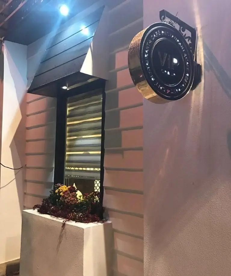 نمای بیرونی شیک رستوران و کافه رستاک در شب، با تابلوی VIP طلایی و مشکی روشن و گل‌های رنگارنگ زیر پنجره.