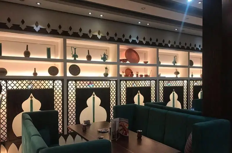 فضای داخلی رستوران رستاک با دکوراسیون سنتی و چشم‌نواز، شامل قفسه‌های تزئینی، ظروف شرقی، نورپردازی گرم و مبلمان راحتی سبز.