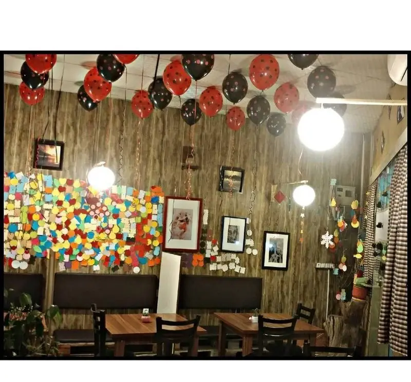 فضای داخلی کافه رستوران دنج با دکوراسیون جشن تولد، شامل بادکنک‌های قرمز و مشکی، دیوارپوش چوبی و میز و صندلی‌های شیک برای لحظات دلنشین.