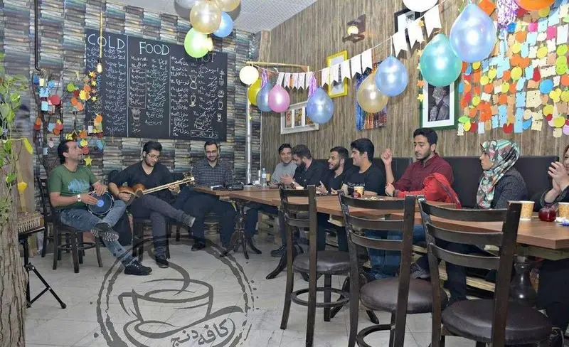 فضای داخلی کافه رستوران دنج با مشتریان در حال لذت بردن از موسیقی زنده و منوی جذاب، محیطی گرم و دوستانه برای دورهمی و مهمانی.