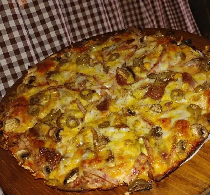 پیتزای خوشمزه قارچ، زیتون، ذرت و تکه‌های گوشت با پنیر فراوان در کافه رستوران دنج. بهترین پیتزای تهران.