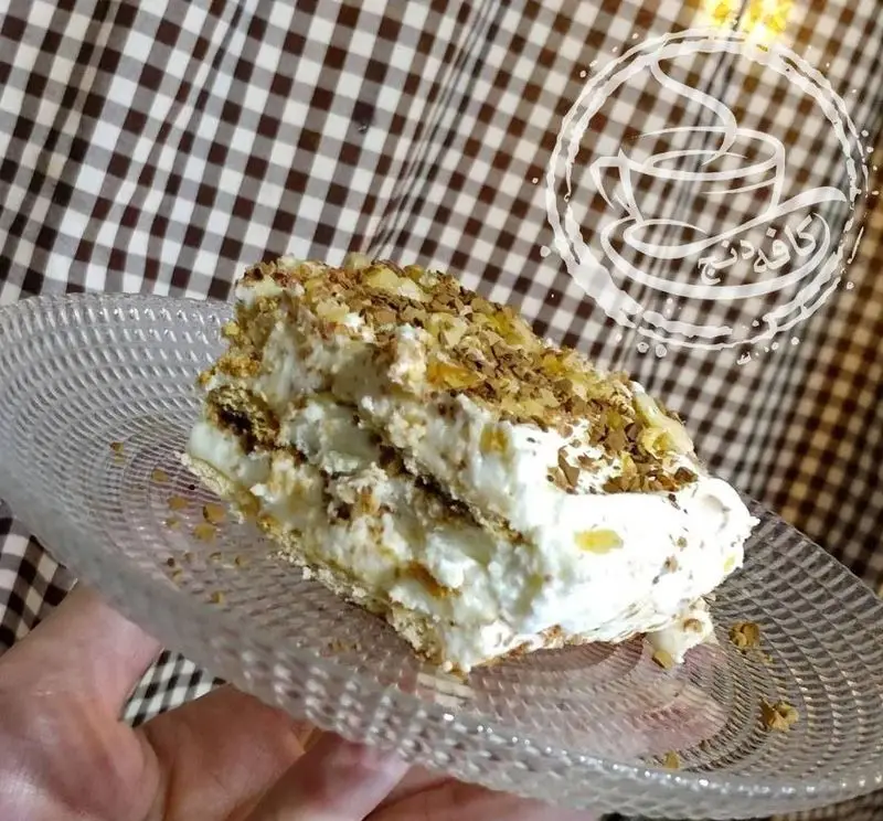 برش کیک دسر لایه ای خوش طعم و خامه ای با تزئین مغزهای خرد شده، تجربه ای لذیذ در کافه رستوران دنج.