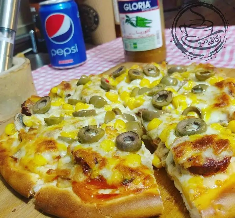 پیتزا ذرت و زیتون خوشمزه کافه رستوران دنج، با پنیر کش‌دار و نان برشته، انتخابی عالی برای تجربه غذای کافه.