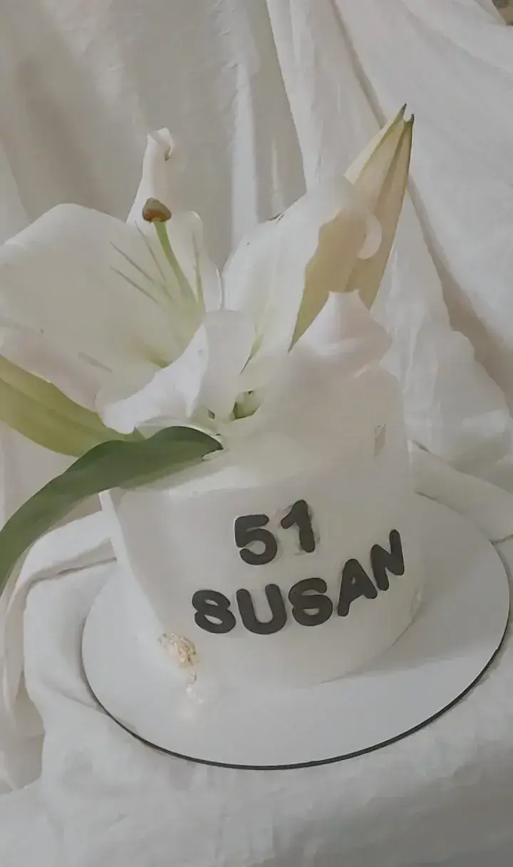 کیک تولد سفید و شیک سوسن به مناسبت ۵۱ سالگی، مزین به گل‌های لیلیوم تازه، طراحی حرفه‌ای کیک ماریا برای لحظات خاص.