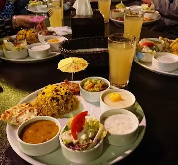 تصویری از میز شام شلوغ در سفره خانه هنرمندان با انواع غذاهای سنتی ایرانی نظیر پلو زعفرانی، خورش، سالاد، پیش‌غذا و نوشیدنی‌های تازه و گوارا.