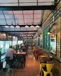 فضای داخلی دنج و مدرن سفره خانه هنرمندان با دیوارهای آجری، سقف شیشه‌ای، نورپردازی صنعتی و میز و صندلی‌های شیک برای مشتریان.