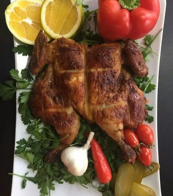 جوجه بریانک کامل طلایی و خوشمزه رستوران، سرو شده با جعفری تازه، لیمو، فلفل دلمه‌ای و گوجه گیلاسی برای بهترین تجربه غذایی.