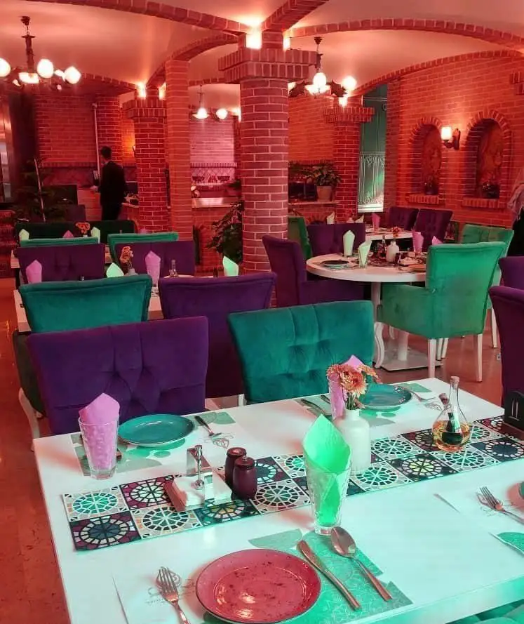 فضای دلنشین و مدرن کافی شاپ سریاس با طراحی داخلی آجری، صندلی‌های سبز و بنفش، نورپردازی گرم و میزهای آماده پذیرایی.