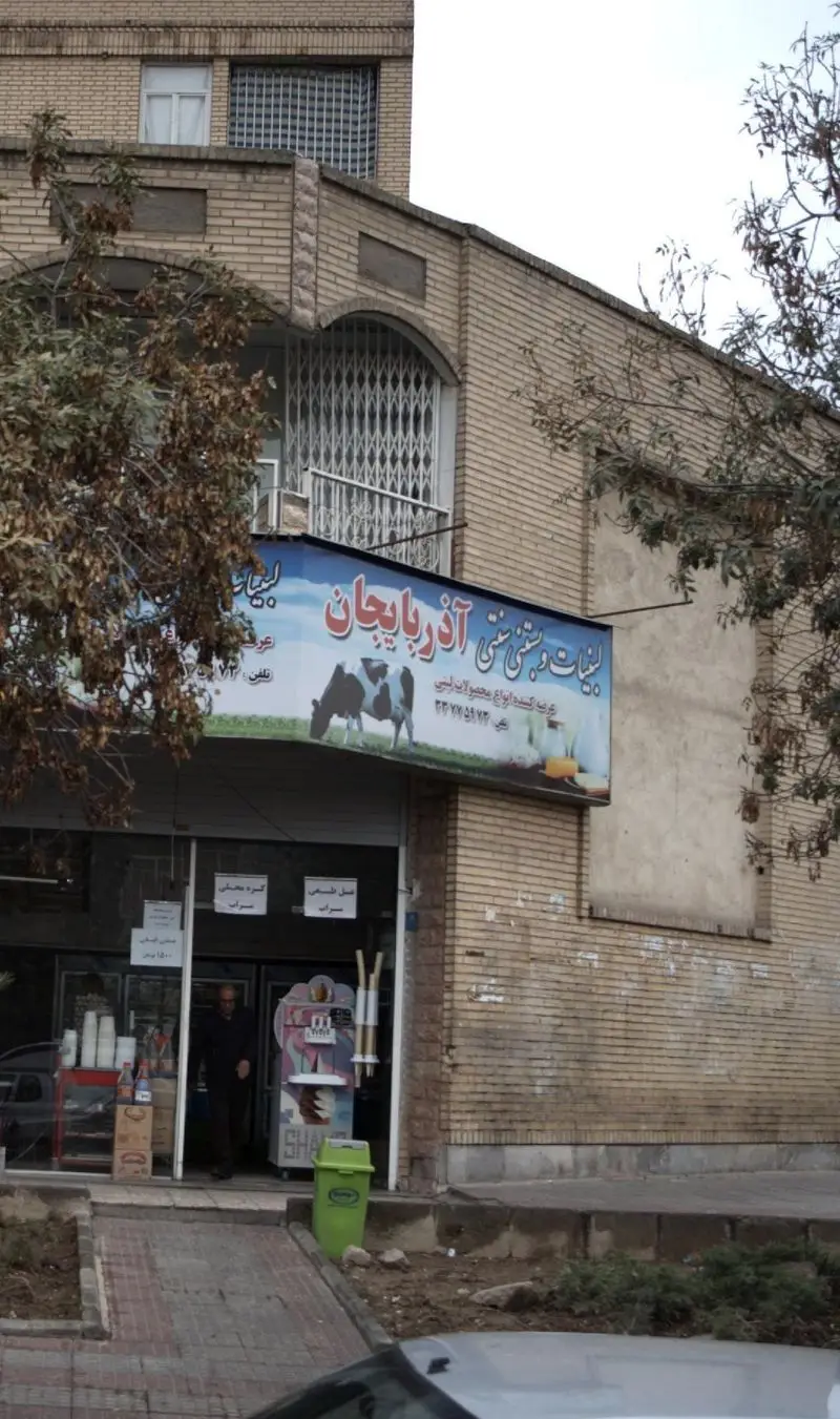 تصویری از نمای بیرونی مغازه لبنیات و بستنی سنتی آذربایجان، با تابلوی بزرگ آبی رنگ حاوی تصویر گاو و محصولات لبنی سنتی و بستنی.