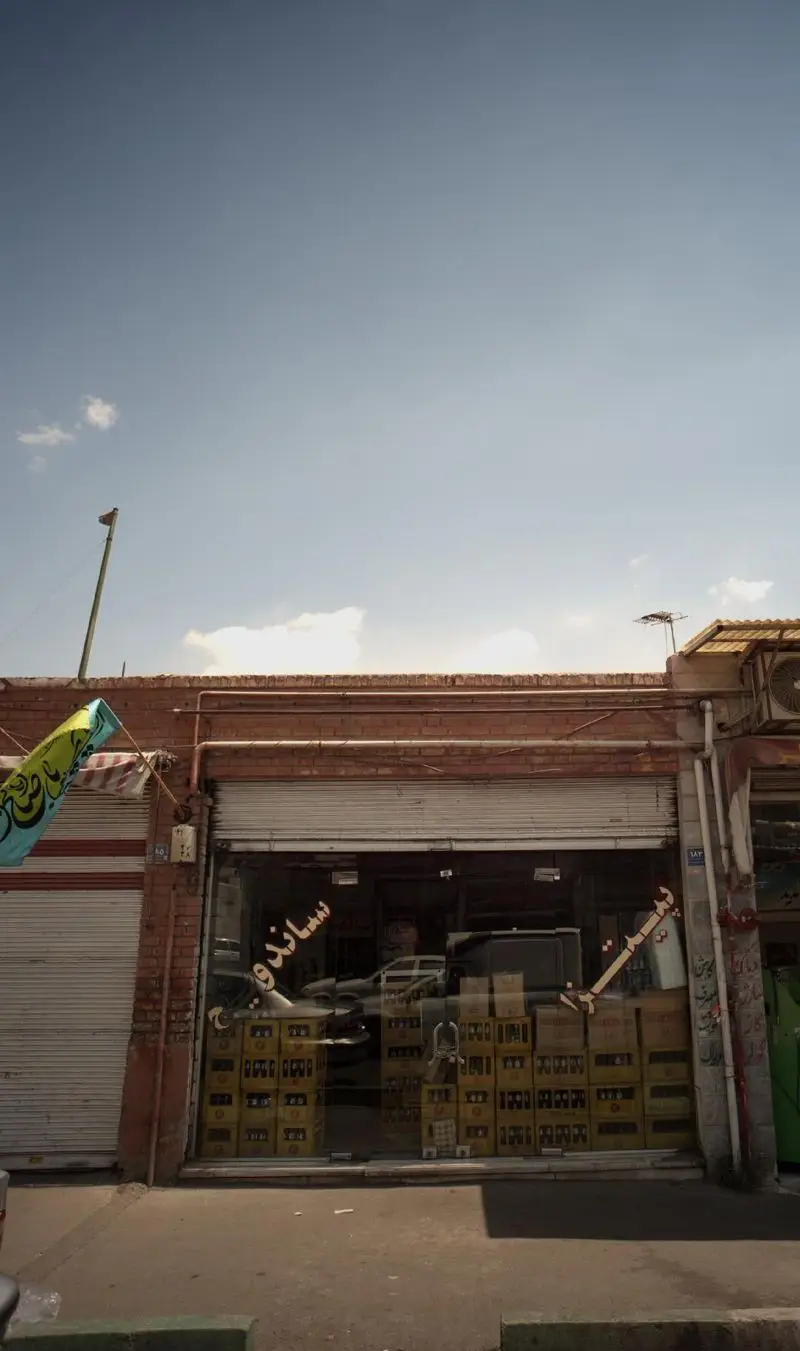 تصویری از نمای بیرونی مغازه پیتزا و ساندویچ در خیابان، با دیوارهای آجری، تابلوی ساندویچ و جعبه‌های نوشیدنی در ویترین.