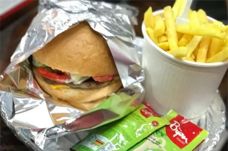 ساندویچ همبرگر آبدار فست فود برگر استار با پنیر، کاهو و گوجه در فویل، کنار سیب زمینی سرخ کرده و سس بیژن.