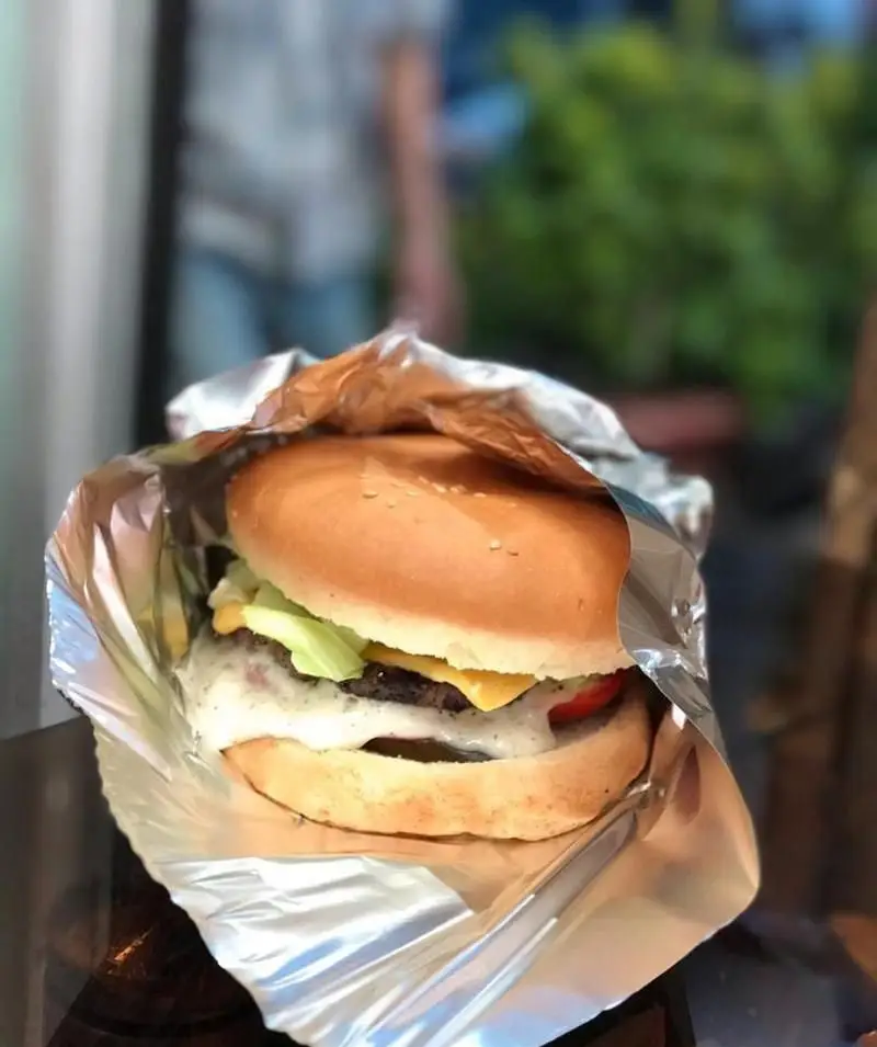 برگر دلپذیر از فست فود برگر استار، مملو از گوشت، پنیر، کاهو، گوجه و سس فراوان، پیچیده در فویل آماده برای سرو. یک وعده غذایی بی‌نظیر.