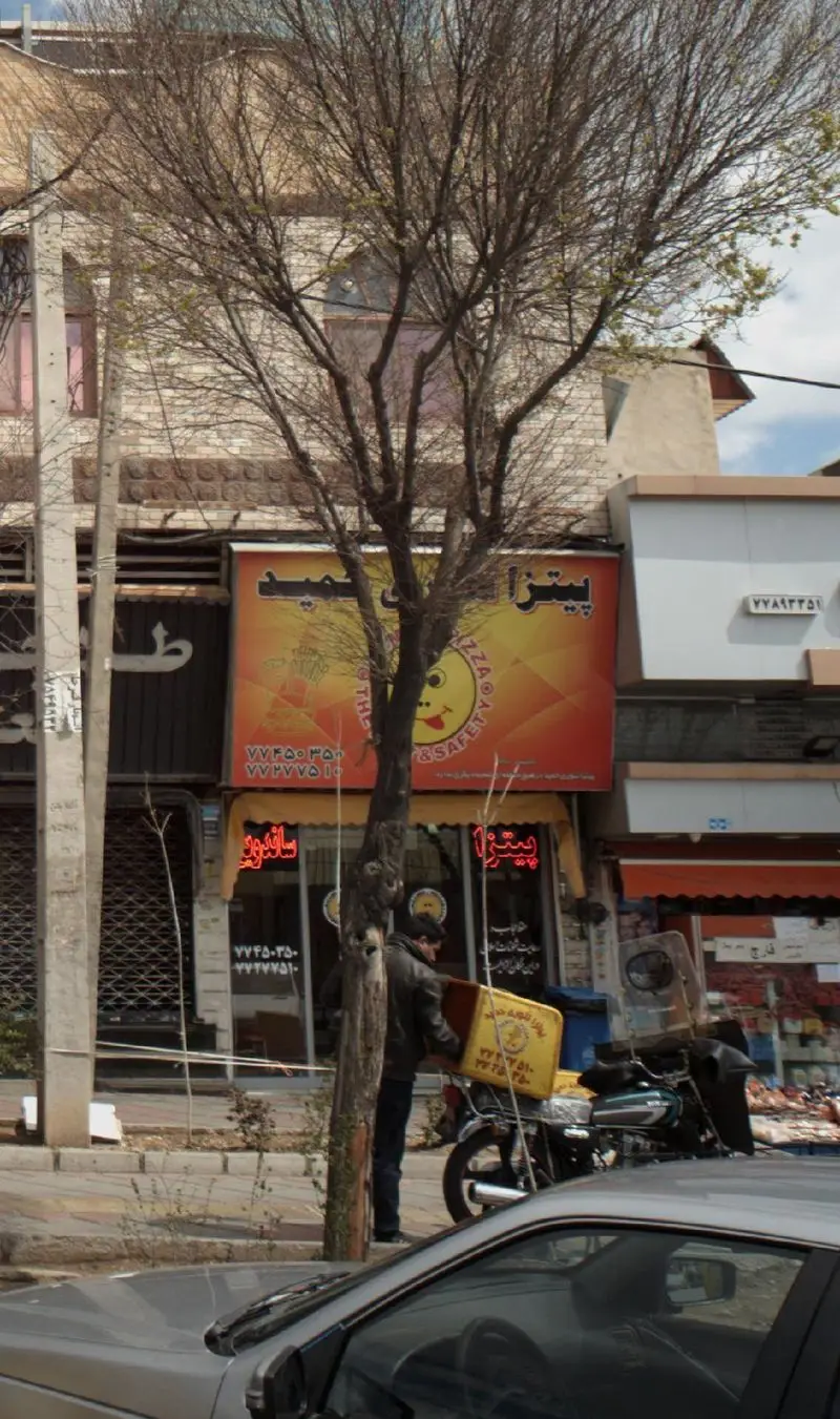 پیتزا فروشی حمید با تابلوی بزرگ و جذاب، پیک موتوری در حال تحویل غذا. خدمات آنلاین و تلفنی برای سفارش پیتزا تنوری.