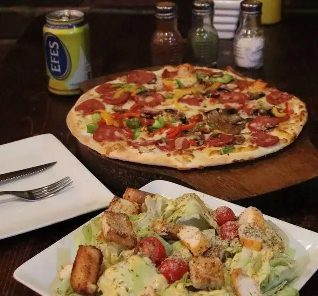 تصویری جذاب از پیتزا یاشار با پپرونی، قارچ و فلفل دلمه‌ای، همراه با سالاد سزار لذیذ با مرغ و نوشیدنی. مناسب برای یک وعده عالی.