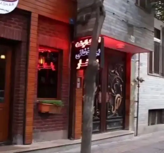 نمای بیرونی پیتزا یاشار، رستوران فست فود با نمای آجری، تابلوی نئونی قرمز و درب فلزی تزئینی در خیابان شهر.