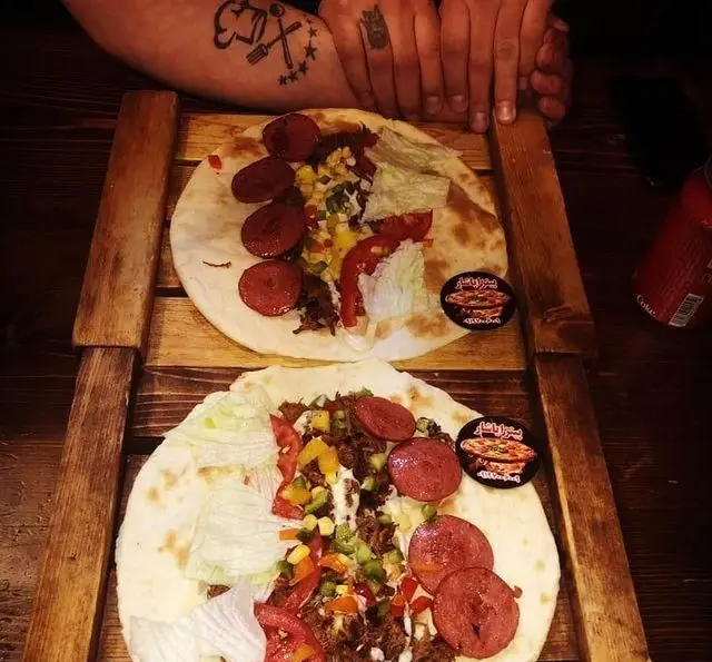 پیتزا ساندویچ‌های پر و پیمان پیتزا یاشار با گوشت، سوسیس، سبزیجات و سس مخصوص، روی تخته چوبی آماده سرو.