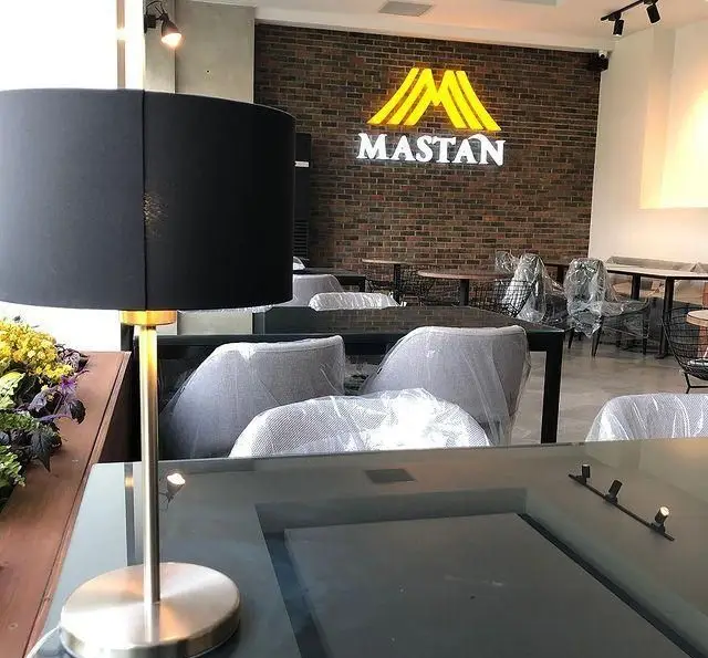 تصویر داخلی کافه رستوران مستان با دکوراسیون مدرن؛ دیوار آجری، لوگوی M درخشان، میز و صندلی‌های نوساز با روکش پلاستیکی.