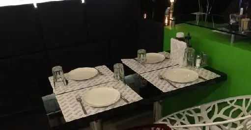 نمای داخلی رستوران ایتالیایی مانلی با میزهای چیدمان شده، صندلی‌های شیک، فضای مدرن و دیوار سبز. مکانی دلنشین برای صرف غذا.