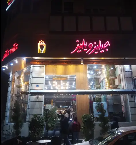 نمای بیرونی فست فود جیلیز ویلیز در شب، با تابلوی روشن و لوگوی برند، نورپردازی جذاب و دید به محیط داخلی رستوران.