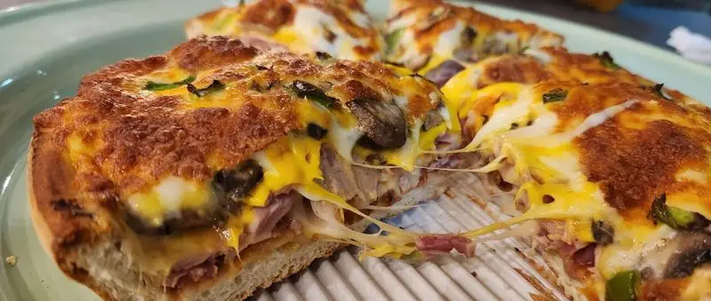 پیتزا سه فر: برشی دلپذیر از پیتزای مغزدار با پنیر طلایی و کشدار، حاوی ژامبون، قارچ و فلفل سبز، لذت طعم و ظاهر