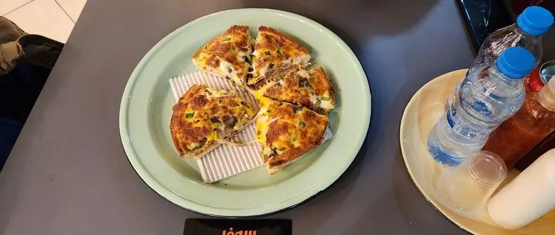 پیتزا سه فر: پیتزای داغ و خوشمزه با پنیر ذوب شده و مخلفات فراوان، به صورت برش‌های مثلثی روی بشقاب سبز رنگ، آماده سرو.